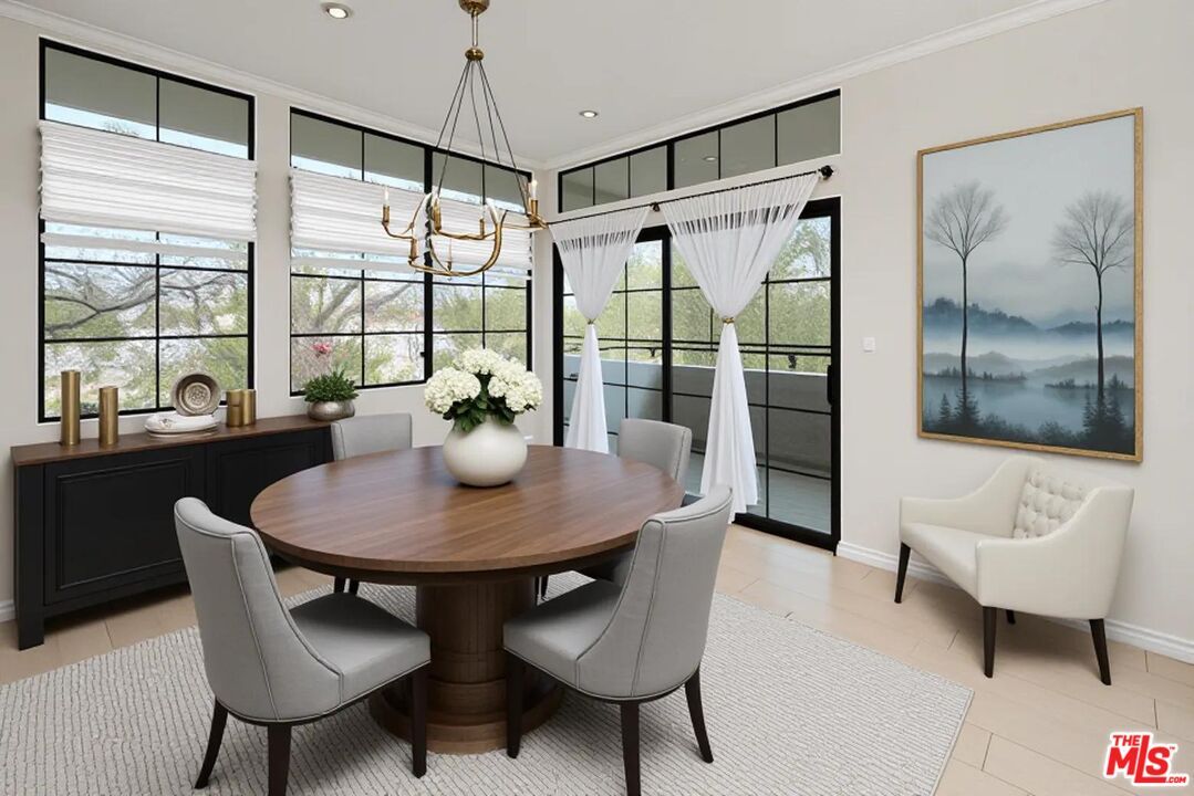 Dining room with round walnut table, gold chandelier, factory-style steel windows and treetop view.