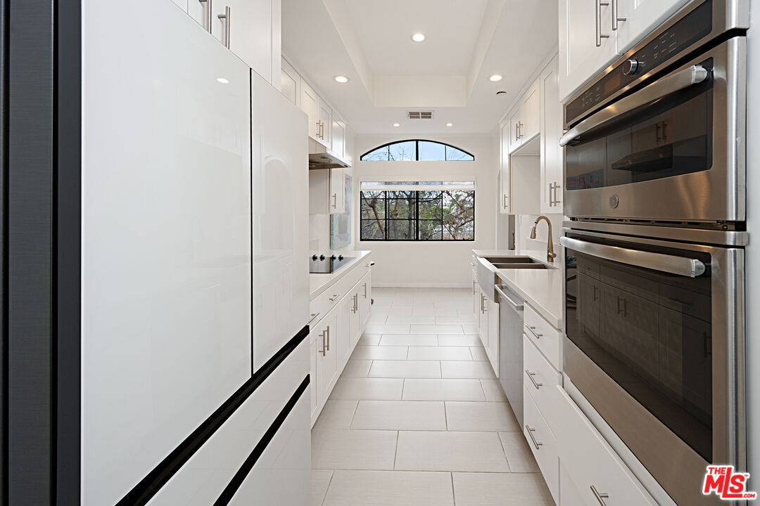 Renovated galley kitchen with white cabinetry, Caesarstone counters, stainless steel double oven and an arched picture window.