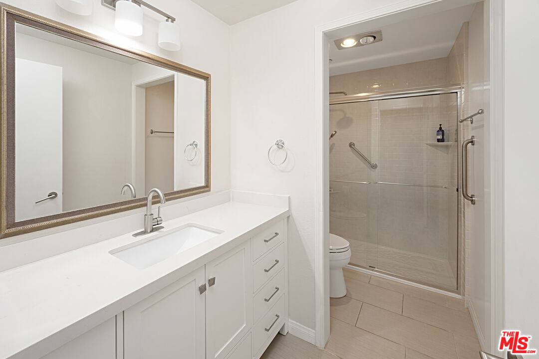 Bathroom with framed mirror, white quartz vanity and separate glass-door tile shower.